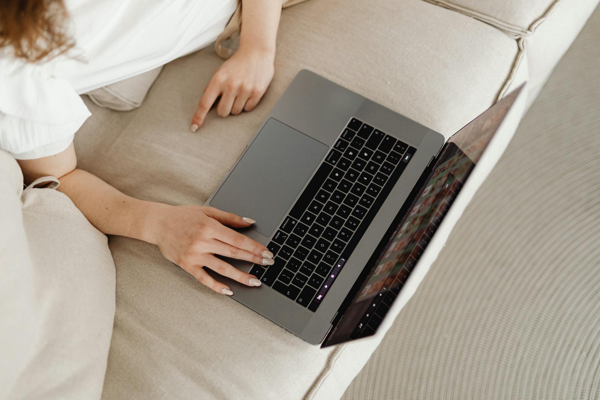 A top down view of a woman leaning on a beige sofa using a MacBook