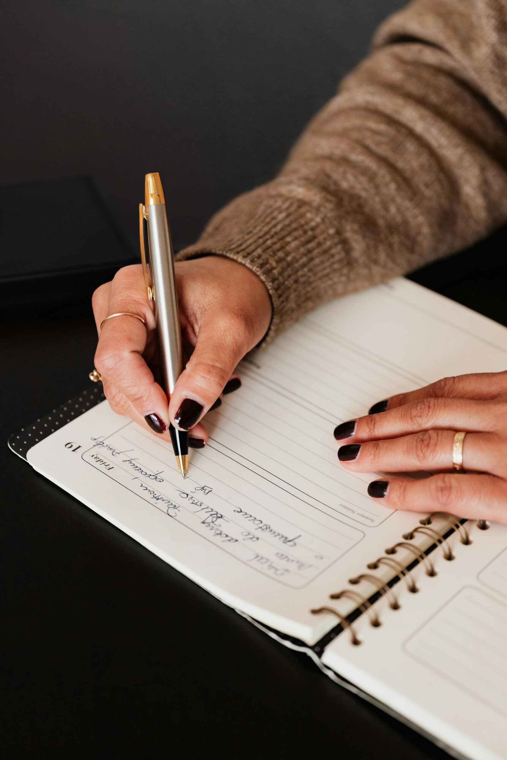 A woman wearing a brown jumper writing in a weekly planner