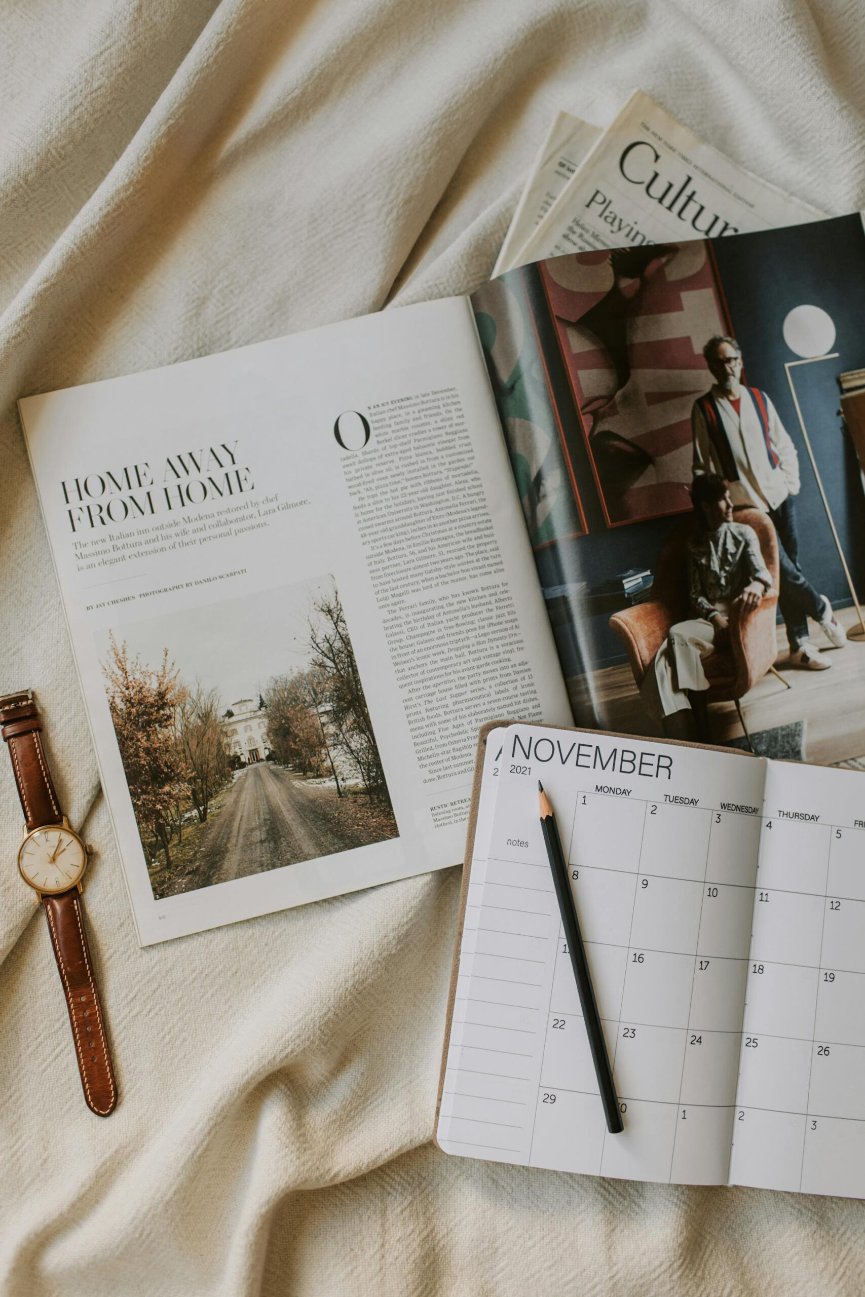 A magazine, a brown leather watch, and a diary open on November